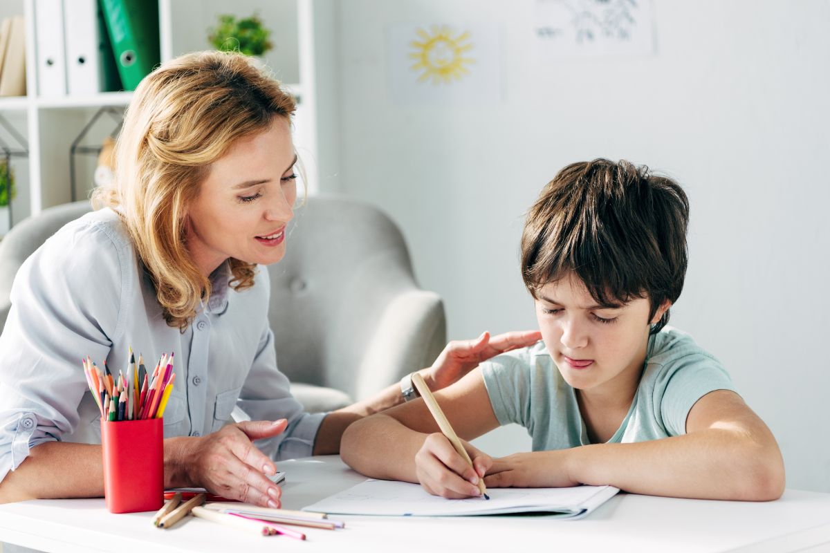 Special education teacher supporting a student as he works on a writing assignment at a table.